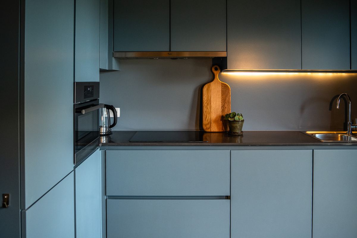 Detail van de keuken met inbouwoven, kookplaat en verlichte werkbladnis