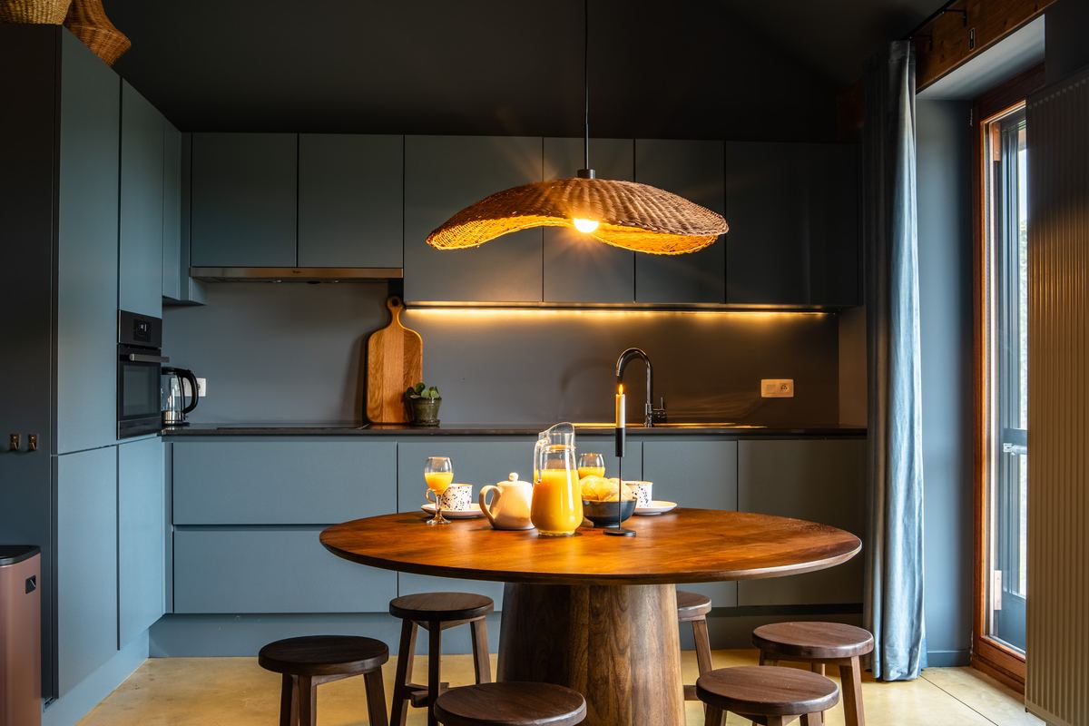 Blauwgroene keuken met ronde eettafel, krukken en rieten hanglamp