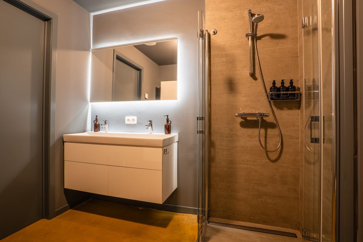Badkamer met dubbele wastafel, verlichte spiegel en glazen douche