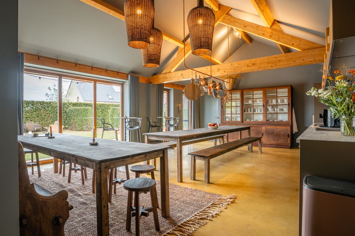 Eetzaal met houten spanten, rieten hanglampen en schuifdeuren naar de tuin