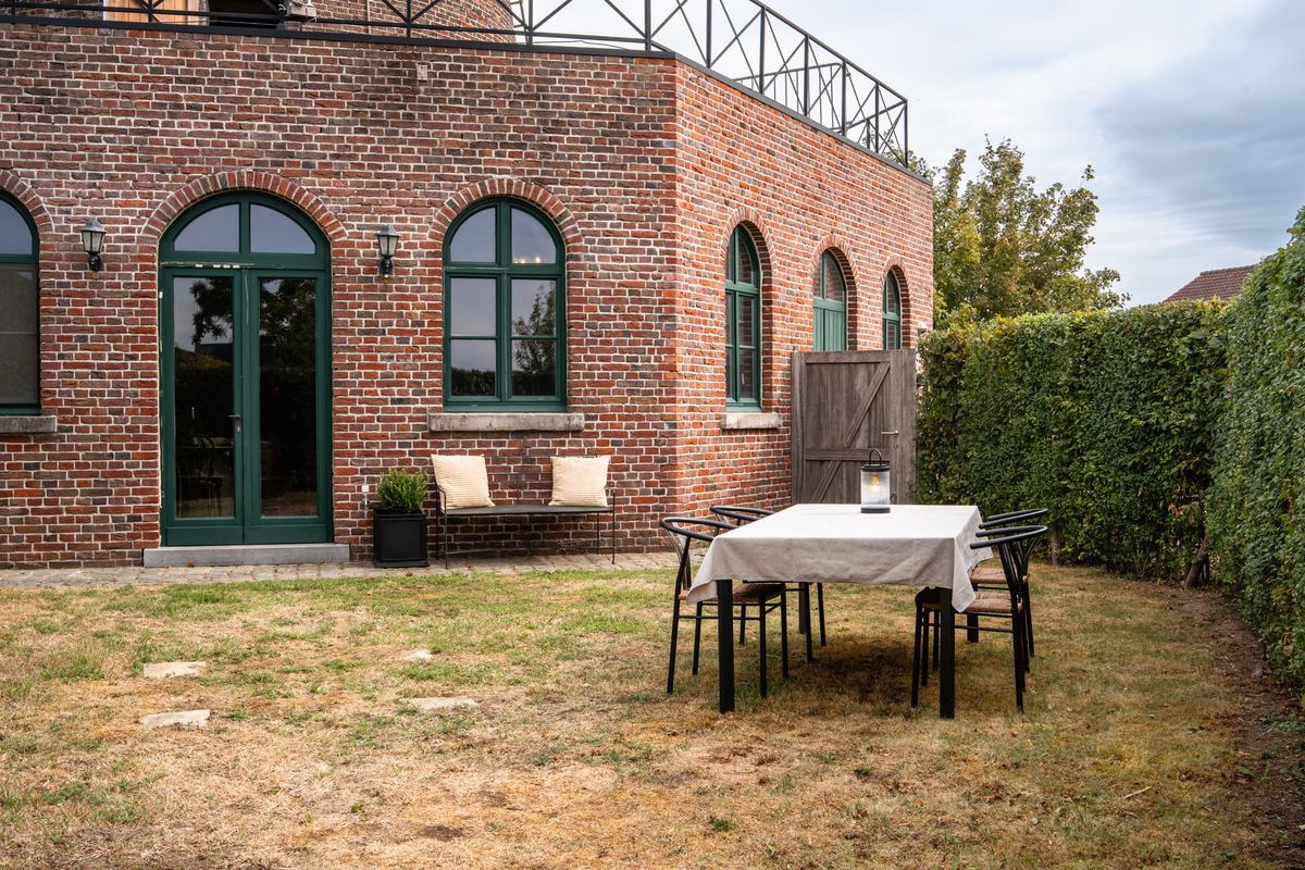 Bakstenen gevel met hoge boogramen en groene deuren, met gedekte tafel in de tuin