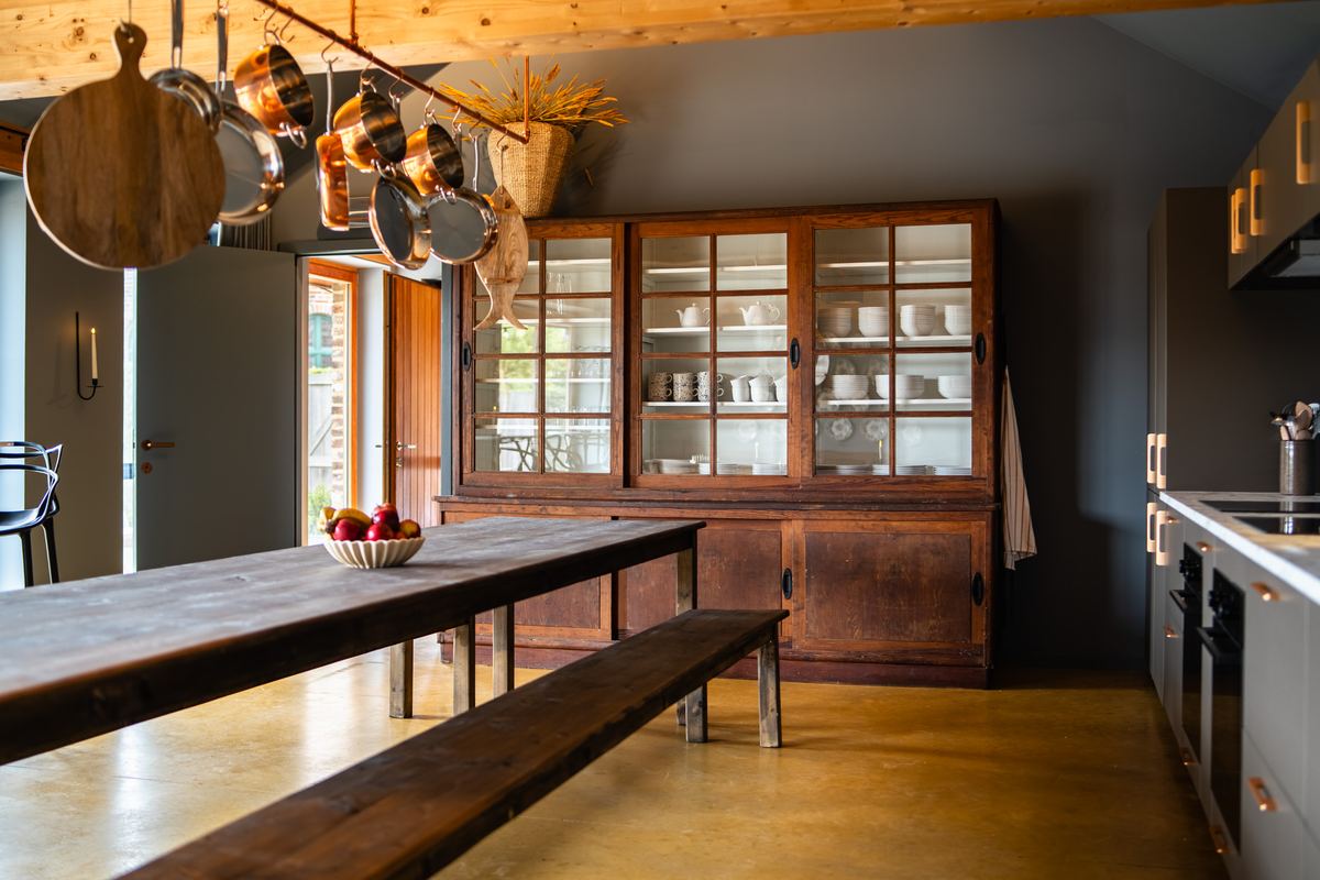 Lange tafel met banken naast een antieke buffetkast met serviesgoed