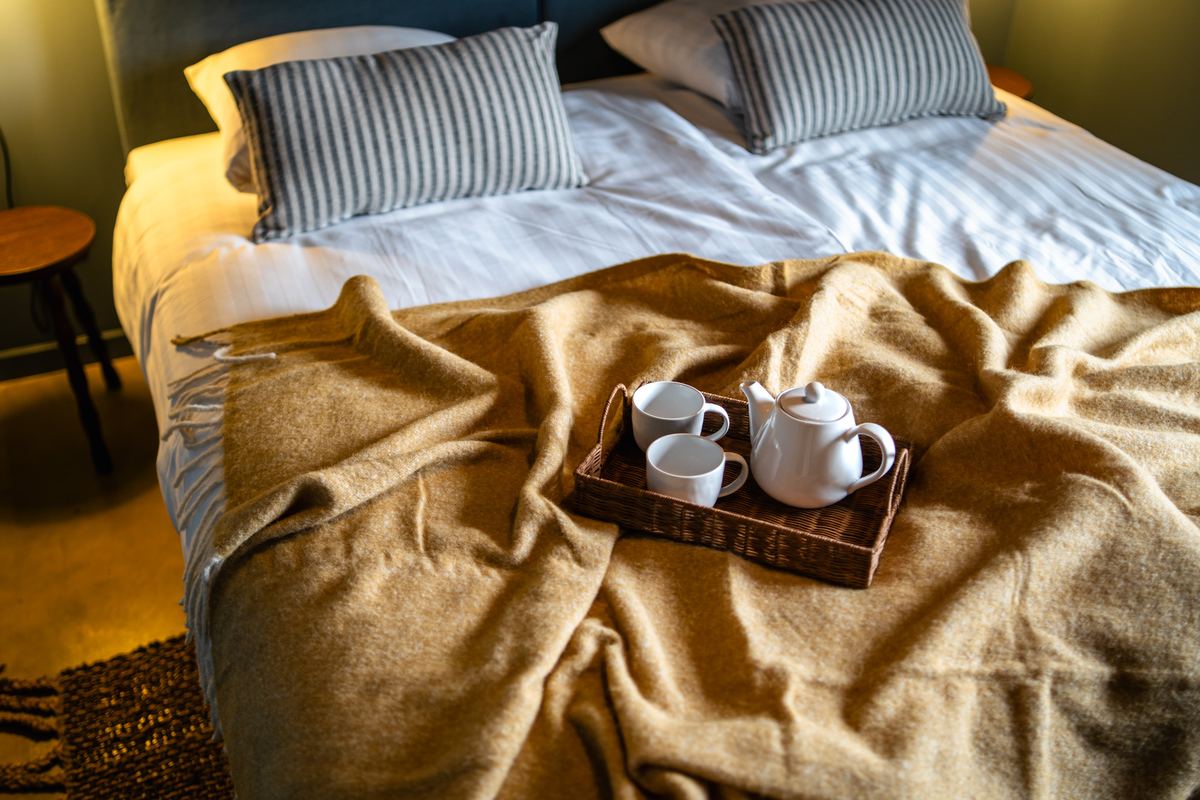 Ontbijtblad met theepot en kopjes op de okergele deken van het bed
