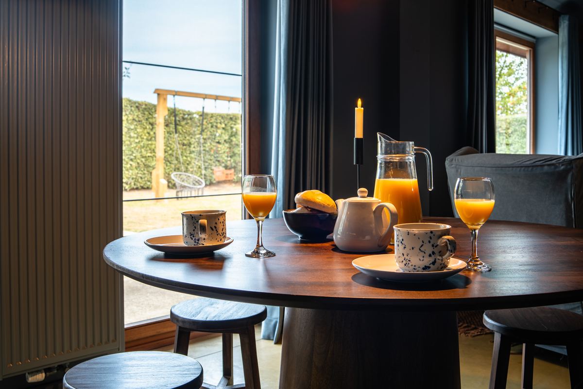 Ronde houten tafel met verse jus d'orange, mokken en kaarsen bij het raam