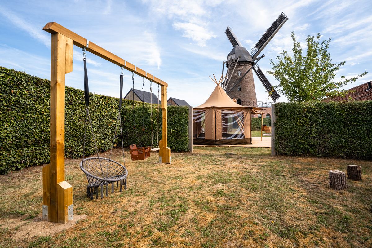 Houten schommelframe met nestschommel in de tuin, met tipi en molen erachter