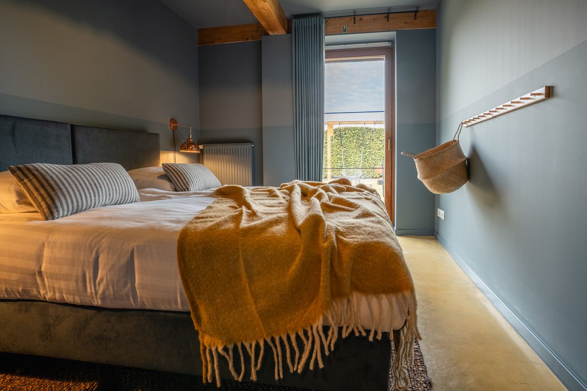 Slaapkamer in blauwgrijs met tweepersoonsbed en okergele wollen plaid