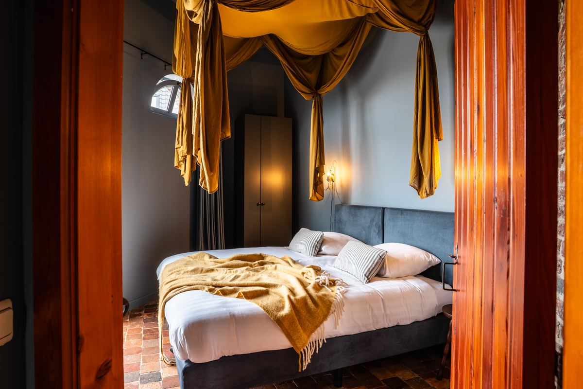 Slaapkamer met okergeel gedrapeerd hemeldoek boven het bed