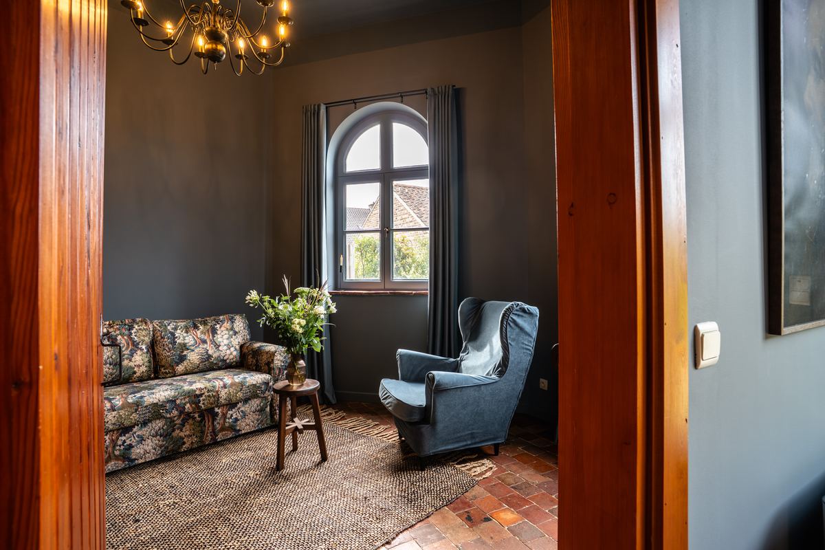 Zithoek met bloemenbank en blauwe oorfauteuil bij een boograam