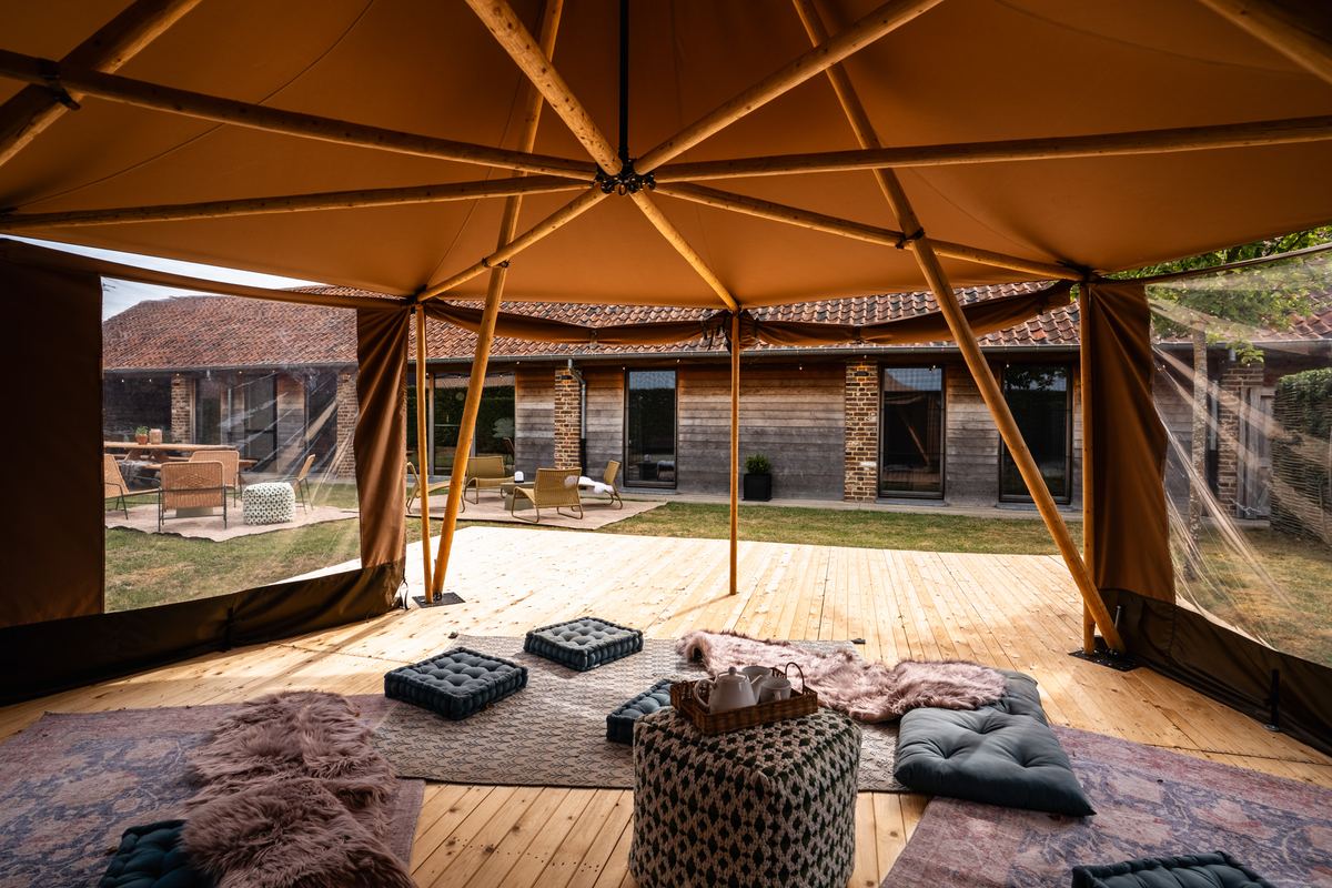 Binnen in de tipi: vloerkussens, kleden en poef op de houten vloer met zicht op de tuin