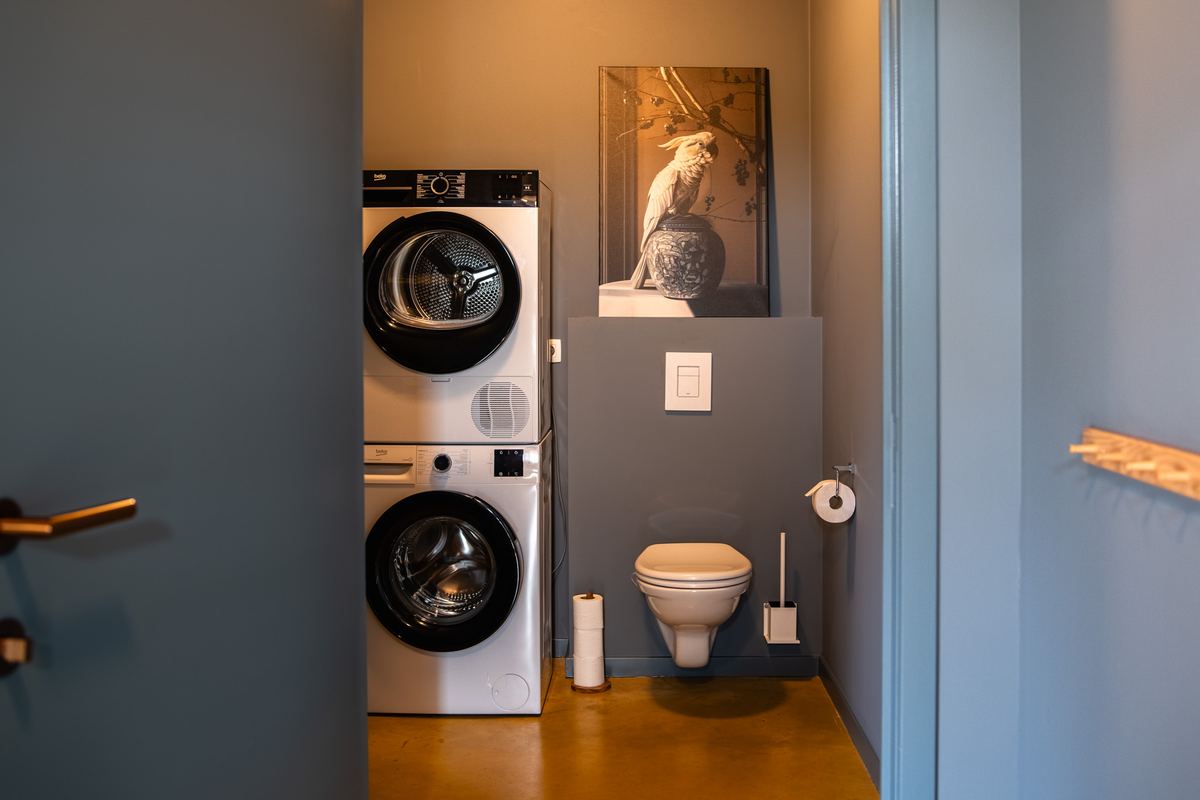 Bijkeuken met wasmachine en droger op elkaar naast een apart toilet